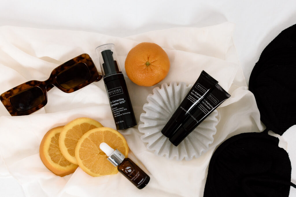 Sunglasses, Oranges & Skincare product on a white sheet.